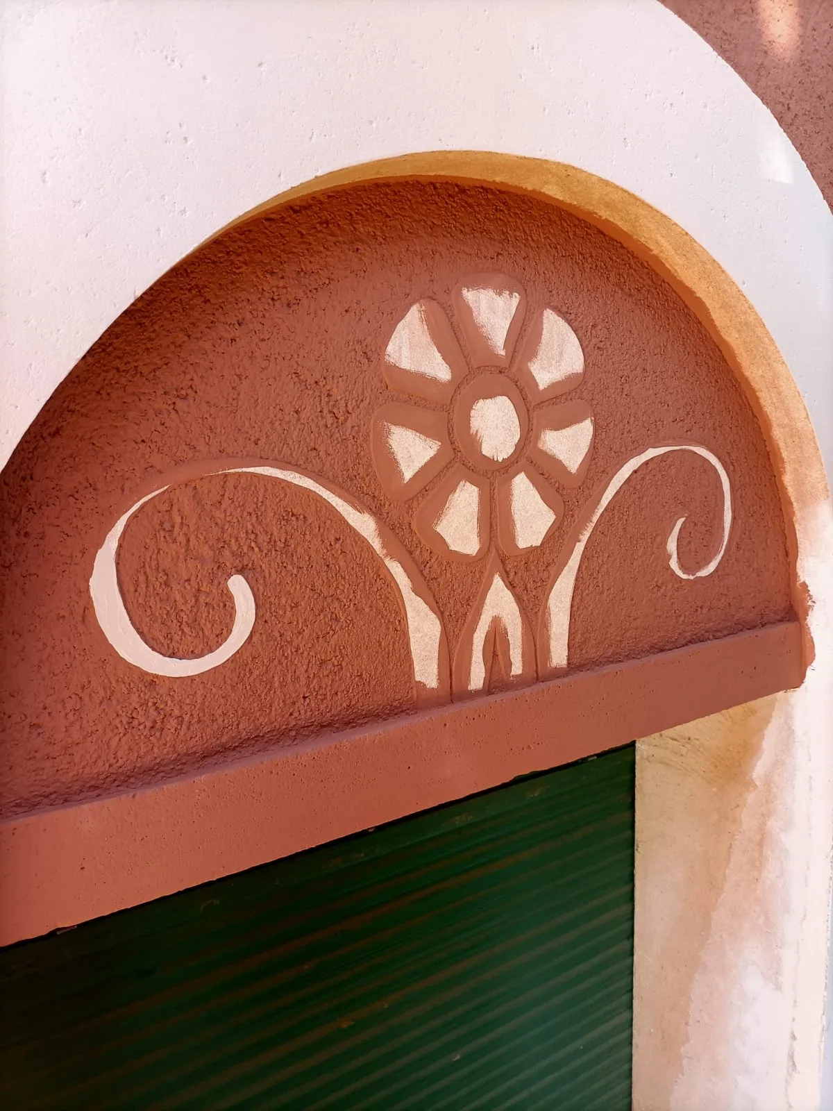 Detalle de arco sobre ventana con relieve de flor y volutas en tono terracota